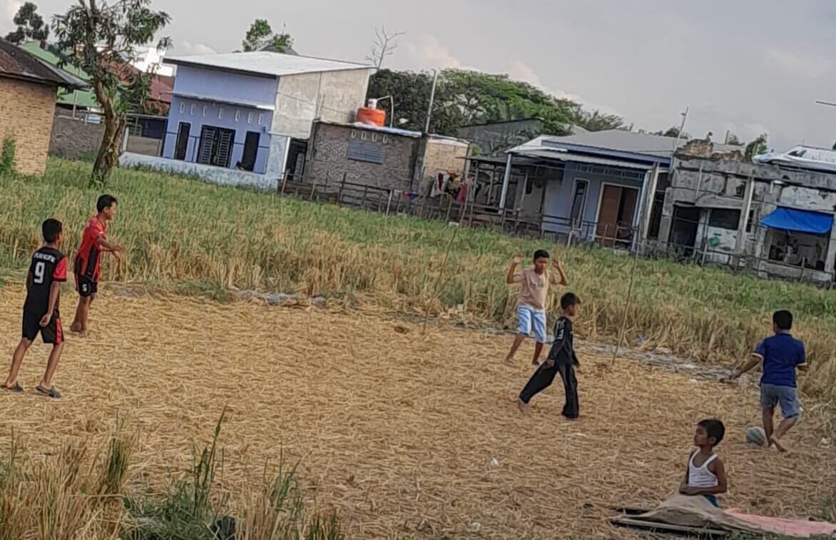 Para bocil bermain sepak bola di areal persawahan yang kering kerontang.
